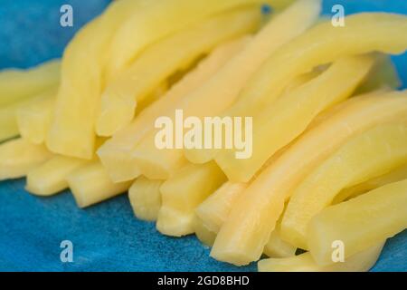 Gelb marinierte Stücke von japanischem Rettich, Daikon auf blauer Platte Stockfoto