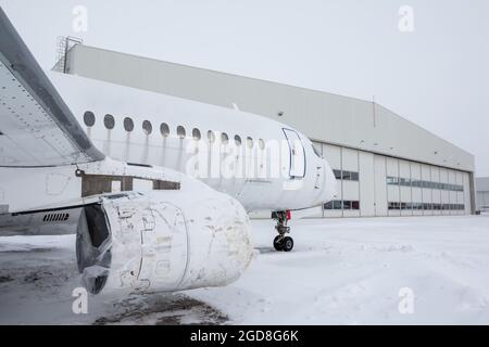 Weißes Passagierflugzeug in der Nähe des Flugzeughangars bei kaltem Winterwetter. Das Düsenflugzeug muss repariert werden Stockfoto