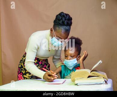 Afrikanische Lehrerin oder Mutter mit Nasenmaske, die einem kleinen Mädchen beim Studium beibringt und hilft, sich in Schule, Bildung und Karriere zu übertreffen Stockfoto