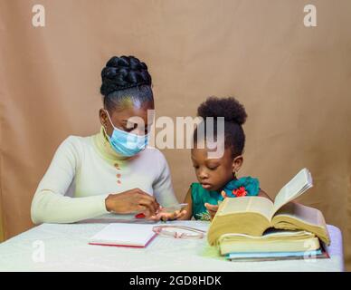 Afrikanische Lehrerin oder Mutter mit Nasenmaske, die einem kleinen Mädchen beim Studium beibringt und hilft, sich in Schule, Bildung und Karriere zu übertreffen Stockfoto