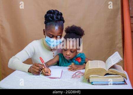 Afrikanische Lehrerin oder Mutter mit Nasenmaske, die einem kleinen Mädchen beim Studium beibringt und hilft, sich in Schule, Bildung und Karriere zu übertreffen Stockfoto