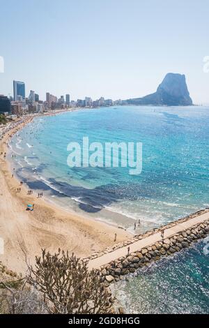 Touristen, die am Strand und Pier entlang der Küste von Calpe mit Blick auf die Felsformation 'ifach', Costa Blanca, Spanien, spazieren Stockfoto