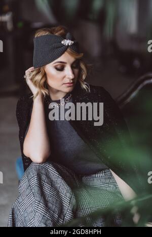 Porträt einer schönen, stilvollen blonden Frau in einem gestrickten Stirnband, einer Jacke und einer Culotte in einem Loft-Innenraum. Weicher, selektiver Fokus, Unschärfe-Effekt. Keine Retouchi Stockfoto