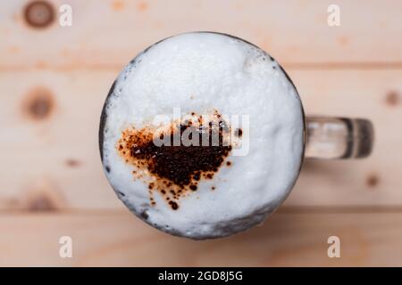 Blick von oben auf Eiskaffeeschaum in der Tasse und Kaffeepulver mit Kaffeebohnen auf Holzboden. Stockfoto