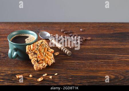 Tasse heißen Kaffee und Kekse mit Nüssen, Sesam und Sonnenblumenkernen in süßem Sirup auf altem Holztisch Stockfoto