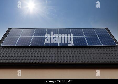 Sonnenkollektoren auf dem Dach vor blauem Himmel mit Sonne Stockfoto