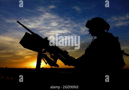 Ein Soldat der US-Armee (USA), der der 1. Infanterie-Division zugewiesen wurde, bemannt ein M2HB-Maschinengewehr im Kaliber 0,50, das auf einem High-Mobility Multipurpose Wheeled Vehicle (HMMWV) montiert war, während einer Patrouille entlang des Logistics Support Area (LSA) Anaconda, in der Nähe des Luftwaffenstützpunkts Balad (ab) im Irak. Das Gebiet wird von Drohungen befreit, sodass Mitarbeiter der Tactical Air Control Party (TACP) einen Luftangriff durchführen können. Das Bild wird gegen die untergehende Sonne silhouettiert. (USAF-FOTO VON SSGT AARON D. ALLMON II 040426-F-7823A-015) Stockfoto