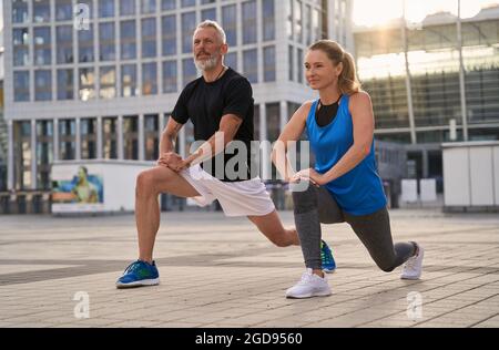 Sportlich reifes Paar, Mann und Frau wärmen sich auf und machen sich bereit, an einem Sommertag gemeinsam in der Stadt zu laufen Stockfoto