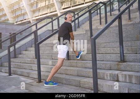 In voller Länge ein Mann mittleren Alters in Sportkleidung und Kopfhörern, der beim Training im Freien Musik oder Podcast hört Stockfoto