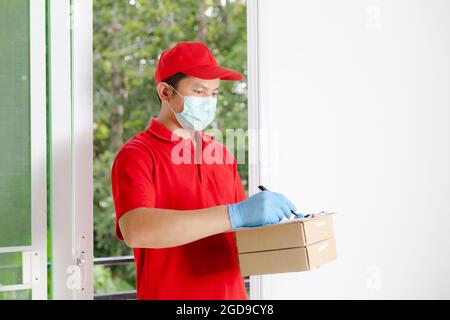 Ein Lieferer in einem roten Kleid hält einen Paketkasten. Stockfoto