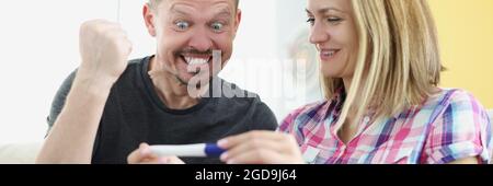 Mann und Frau freuen sich und halten positive Schwangerschaftstest zu Hause Stockfoto
