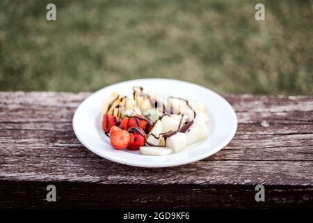 Köstlicher Obstsalat mit Schokoladenüberzug auf Holzbank Stockfoto