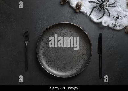 Festliche Halloween Tischunterlage mit schwarzem Tellerbesteck, Spinne und Netz auf schwarzem Hintergrund. Blick von oben. Speicherplatz kopieren. Stockfoto