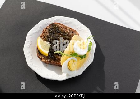 Schwarzer Kaviar auf einem festlichen Sandwich mit Eiern, Zitrone, Grün. Gesund reich an Antioxidantien leckere Speisen. Selektiver Fokus. Stockfoto