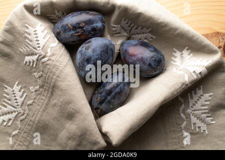 Reife dunkelviolette Pflaumen, Nahaufnahme, auf Leinenserviette, Draufsicht. Stockfoto