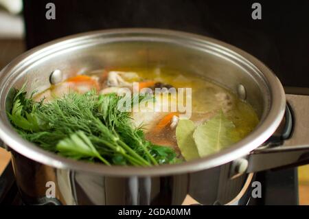 Hinzufügen von Kräutern, Lorbeerblättern und Gewürzen in die Brühe. Wasser mit Gemüse und Fleisch kocht in einem Topf. Stockfoto