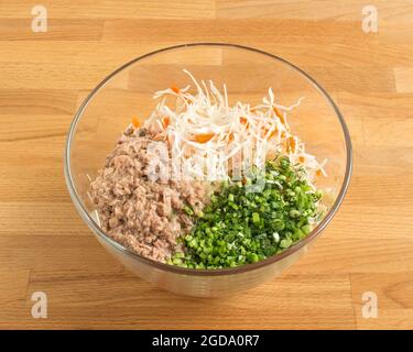 Zutaten in einer transparenten Fischsalatschüssel. Konserven, gehackte grüne Zwiebeln, frischer Kohl. Stockfoto