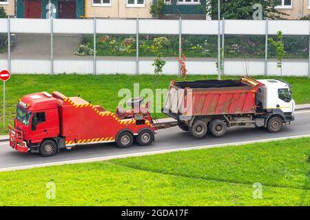 Leistungsstarke große rote semi-Evakuierung LKW-Schlepper Schlepper mit angebautem gebrochenen evakuierten LKW mit Körper fahren auf Stadt Autobahn Stockfoto