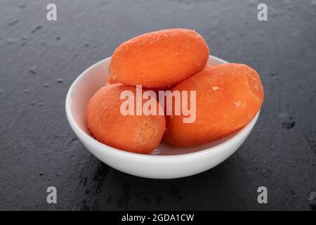 Mehrere leuchtend orange saftige, natürliche Mini-Karotten in einer weißen Keramikschale, Nahaufnahme, auf einem Schiefertafel. Stockfoto