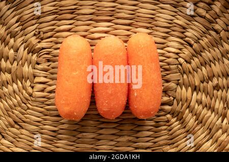 Mehrere leuchtend orange Natur-Mini-Karotten, Nahaufnahme, auf einer Strohmatte, Draufsicht. Stockfoto