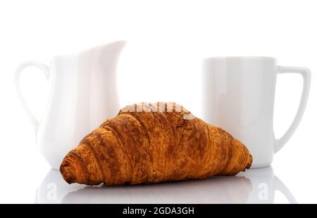 Ein frisch gebackenes duftendes Croissant mit weißem Milchkännchen und Tasse, Nahaufnahme, isoliert auf Weiß. Stockfoto