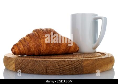 Ein frisch gebackenes duftendes Croissant auf einem Holztablett mit einer weißen Tasse, aus der Nähe, isoliert auf Weiß. Stockfoto