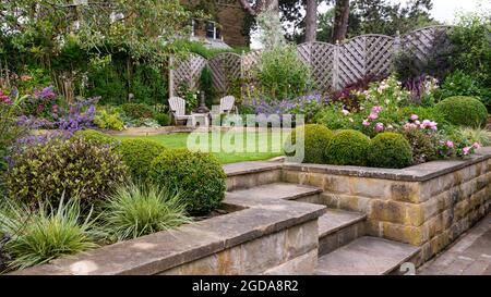 Farbenfroh gestalteter privater Garten im Sommer (zeitgenössisches Design, Terrasse & Terrasse, erhöhte Betten, Sitzplätze auf der Terrasse, Rasen) - Yorkshire, England, Vereinigtes Königreich. Stockfoto