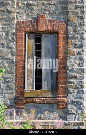 Rotes Ziegelfenster eines alten Schlosses in einer Wand aus natürlichem grauen Stein. Gewölbte Konstruktion. Sommersonntag. Nahaufnahme Stockfoto