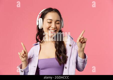 Lifestyle-, Musik- und Technologiekonzept. Nahaufnahme des sorgenfreien, fröhlichen lächelnden asiaten, die den neuen Song der Lieblingssängerin genießen und mit dem sie tanzt Stockfoto