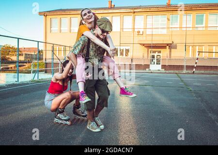 Eine Gruppe von Freunden, die draußen rumhängen. Ein Mädchen reitet zurück ihre Freundin, andere reitet hinter auf Rollen. Positive Vibes Stockfoto