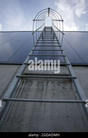 Notausfluß auf dem Industriegebäude oben, Ansicht von unten. Handläufe aus Edelstahl, Dachleiter. Detailansicht der Treppe mit Sicherheitskäfig. Gebäude CO Stockfoto