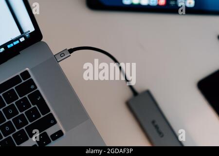 Draufsicht auf einen grauen Laptop auf dem Schreibtisch mit eingestecktem schwarzen USB-Kabel Stockfoto