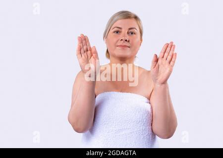 Schüchterne blonde Frau zeigt und wirbt für ein Produkt für die Handhautpflege, die ihre Hände hochhält, mit gedrehten Handflächen zur Kamera. Stockfoto