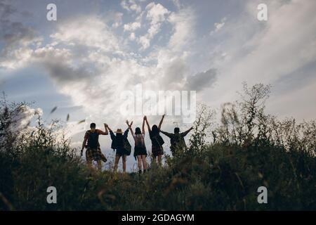 Silhouetten von Menschen, jungen Männern und Frauen treffen Sonnenuntergang im Freien, im Sommerwald, Wiese. Aktiver Lebensstil, Freundschaft, Pflege, Ökologie Konzept Stockfoto