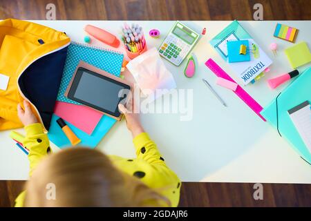 Zurück zur Schule. Obere Ansicht des modernen Mädchens mit Arbeitsbüchern, Schreibwaren, Lehrbuch, Tablet-pc und Rucksack-Verpackung für die Schule am weißen Tisch zu Hause. Stockfoto