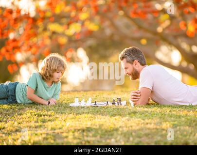 Glückliche Familie von Vater und Sohn Kind spielen Schach auf grünem Gras im Park im Freien, Genie Stockfoto