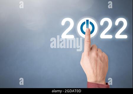 Fingerdruck der blauen Start 2022-Taste auf der virtuellen Benutzeroberfläche auf grauem Hintergrund mit Platz für Text. Konzept des neuen Jahres. Geschäftsmann drücken 202 Stockfoto