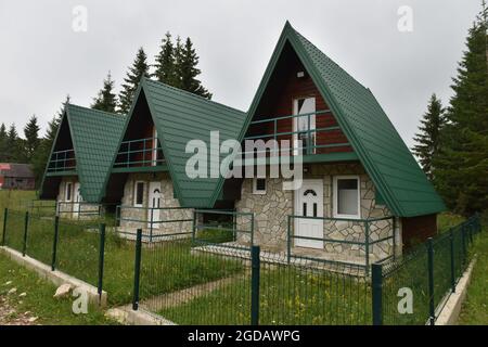 Kleines Haus im Wald in den Bergen. Ferienwohnung - Holzhütte im Wald im frühen Frühjahr mit grünem Gras auf dem Hinterhof und Wald in Stockfoto