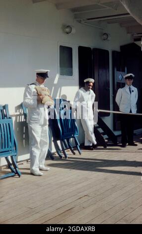 Ein uniformierte Offizier, der darlegt, wie man eine Rettungsweste oder ein persönliches Flotationsgerät auf dem Kreuzfahrtliner SS Maasdam der Holland America Line anlegt und trägt, während er 1959 in New York, USA, im Dock war. Hier würde ein Leinwandbeutel flexible wasserdichte Zellen enthalten, die mit Kapok gefüllt sind. Das Gerät ist nutzbringend nummeriert (hier 32.12), um eine Organisation an Bord des Schiffes und jeden Rettungsversuch zu unterstützen. Dieses Gerät (PFD, Rettungsweste, Rettungsring, Rettungsgurt, Mae West, Rettungsweste, Rettungsschwimmer, Korkjacke, Schwimmhilfe oder Schwimmanzug) wird getragen, um Ertrinken zu verhindern – ein Vintage-Foto aus den 1950er Jahren. Stockfoto