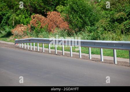 Rote Straßenreflektoren entlang der Straße. Metalleinzäunung von Barriere-Typ, Nahaufnahme. Straßen- und Verkehrssicherheit. Reflektierende Farbe auf dem Schild. Mittlere Barriere Stockfoto
