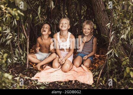 Lachende Kinder spielen in einer Hütte aus Zweigen und Blättern. Holzhaus im Wald Stockfoto