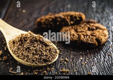 Holzlöffel in rustikaler Küche verwendet, mit pulverförmiger Schokolade. Rustikaler Holztisch, hausgemachte Schokoladenkekse im Hintergrund Stockfoto