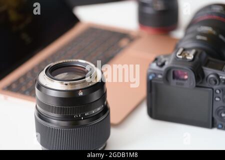 Objektive und Kamera liegen auf dem Tisch in der Nähe des Laptops Stockfoto