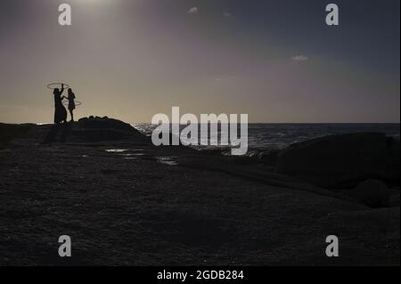 Hula-Hoop-Spiel am Bakoven Beach bei Sonnenuntergang an der Atlantikküste von Kapstadt in Südafrika Stockfoto
