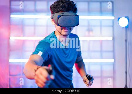 Junger Mann, der Videospiel spielt, indem er eine VR- oder Virtual-Reality-Brille trägt und Joysticks in den Händen hält - Konzept der modernen Gaming-Technologie Stockfoto