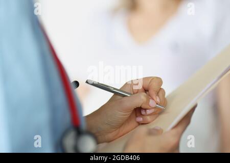 Arzt, der die medizinischen Dokumente des Patienten mit einem Kugelschreiber in der Nähe der Station ausfüllt Stockfoto