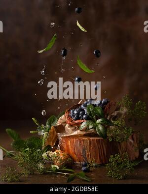 Stillleben mit Blaubeeren und grünen Blättern. Beeren und Blätter fallen Stockfoto