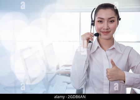 Der asiatische Callcenter-Mitarbeiter im Portrait-Stil Daumen nach oben. Helpdesk-Support Telefonanruf Kundendienst weibliches Personal lächelt mit Headset gutes Servicekonzept mit sp Stockfoto