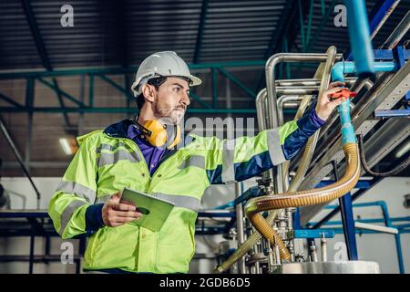 Junger lateinamerikanischer Ingenieur, der in einer schweren Industriefabrik arbeitet. Arbeiter kontrollieren Ölgas-Wasserleitung im Werk. Stockfoto