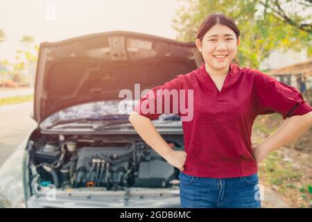 Portrait glückliche Frauen stehen vor zerbrochenen Unfällen Auto offene Haube lächelnd wartet Autoversicherung am Straßenrand ohne Sorge. Stockfoto